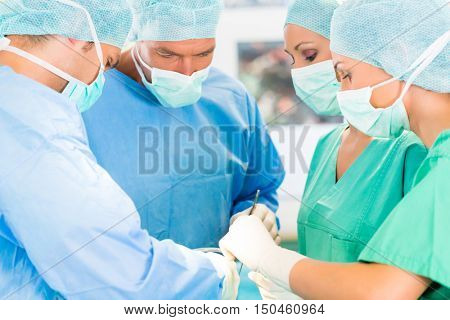 Hospital - surgery team in the operating room or Op of a clinic operating on a patient, perhaps it's an emergency a assistant holding a cotton swap forceps