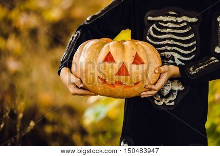 Hands Boy in halloween masquerade costume ih light from pumpkin head. Close-up