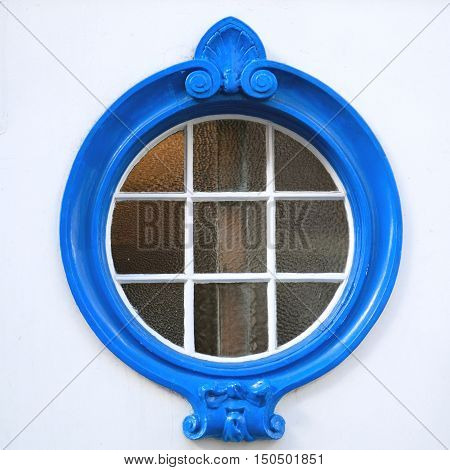 Architectural detail of beautifully decorated blue wooden circle window on a building with facade painted in white