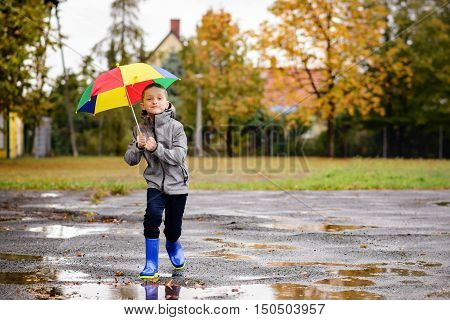 Boy In Rubber Blue Rainboots Jumping To Dirty Puddle