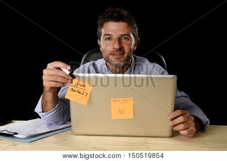 corporate portrait of happy successful businessman in shirt and tie smiling at office desk working with laptop computer isolated on black background confident and trustful in business success concept