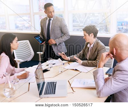 Professional mature adult mixed race well dressed businessman conducting a presentation in a bright modern conference room while holding and using a tablet in his presentation.