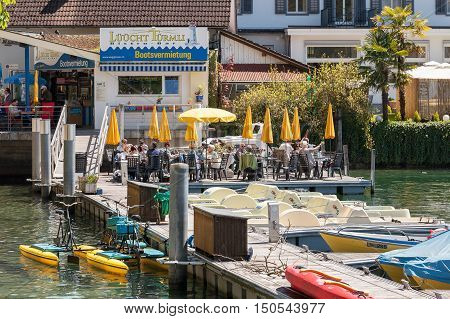 WEGGIS SWITZERLAND - MAY 05 2016: Unidentified guests of the bistro bar enjoys food and drinks. Guests sit at tables arranged on the platform at the Jetty on the Lake Lucerne