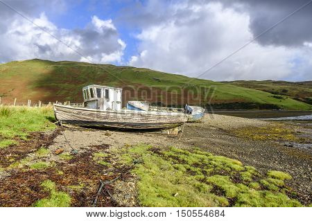 Sun shines on the peeling paint of two old abandoned wooden boat wrecks on the shore of Loch Harport on Isle of Skye Scotland