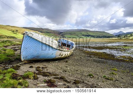 Beautiful Isle of Skye Scotland landscape. Old abandoned wooden boat wreck with peeling blue paint on the shore at Loch Harport at low tide