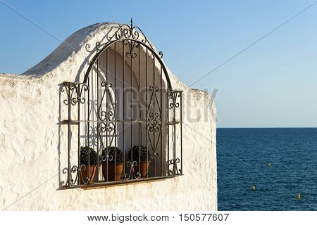 Typical spanish grated window in a white wall house Mediterranean Sea in Background. Roc de Sant Gaieta Tarragona Catalunya Spain.