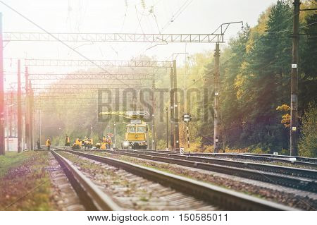 Workers in orange raincoats repair railroad on sunny day