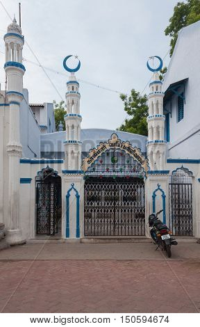 Madurai India - October 21 2013: Entrance with four short minarets to the Kajimar Mosque is painted white and blue. Black and white iron fence forms the gate