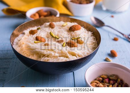 Indian sweet sutarfeni or sutar feni or firni or seviyan or laccha, shredded, flaky-rice-flour roasted in ghee, blended with melted sugar to form a cotton candy, topped with pistachio and almonds