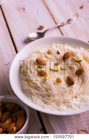 Indian sweet sutarfeni or sutar feni or firni or seviyan or laccha, shredded, flaky-rice-flour roasted in ghee, blended with melted sugar to form a cotton candy, topped with pistachio and almonds