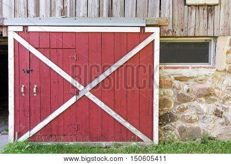 Partially open red barn door in a weathered barn. Traditional white framing weathered wood field stone texture and nostalgia.