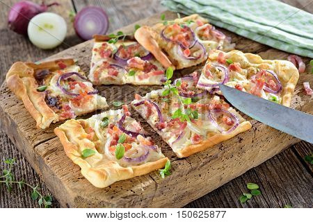 Hot baked tarte flambee from Alsace with onions, bacon and sour cream served on a shabby wooden cutting board