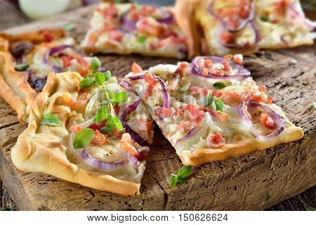 Hot baked tarte flambee from Alsace with onions, bacon and sour cream served on a shabby wooden cutting board
