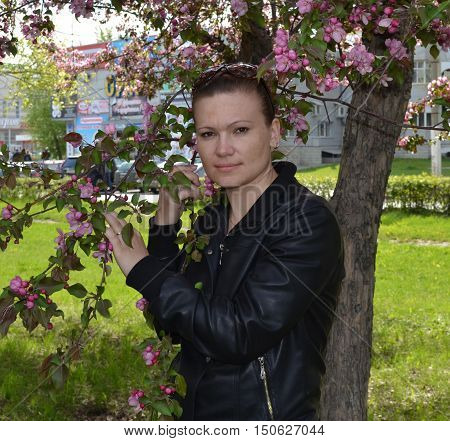 Young girl standing near blooming apple tree thoughtfully looks ahead