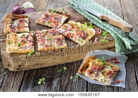 Hot baked tarte flambee from Alsace with onions, bacon and sour cream served on a shabby wooden cutting board
