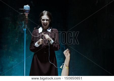 Portrait of a young girl with knife and drop counter in school uniform as killer woman against school board . The image in the style of Halloween and Addams family