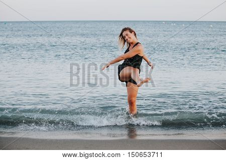 Young girl kicking the sea water in sportswear.