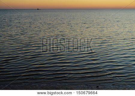 Tranquil harbour with lighthouse at the horizon.