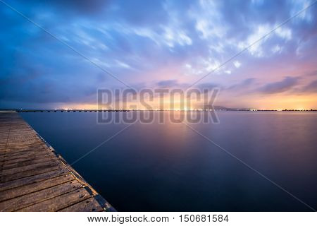 Distant city lights watched from a wooden pier.