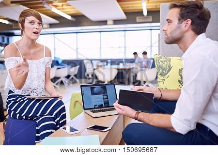 Intelligent businesswoman using her hands while explaining her business proposal to her male business partner in a modern bright and colourful co working environment.
