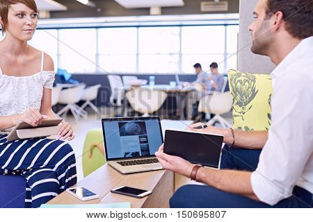 Beautiful young caucasian business woman holding a modern tablet while paying close attention to her professional male financial advisor during their meeting in a modern co working space.