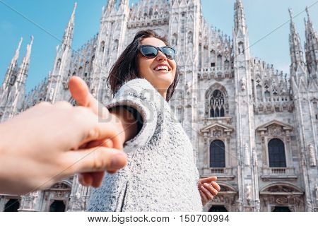 Smiling woman hold his boyfriend hand on Duomo di Milano background