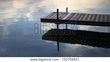 Dock on a lake with clouds reflected in water