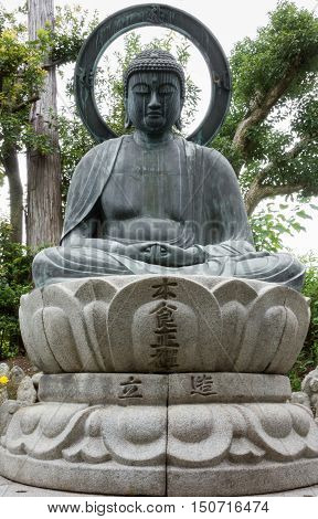 Kyoto Japan - September 15 2016: At the Shinnyo-do Buddhist Temple the stone statue of the meditating or Amithabha Buddha stands in the garden. He sits on lotus and has big halo.