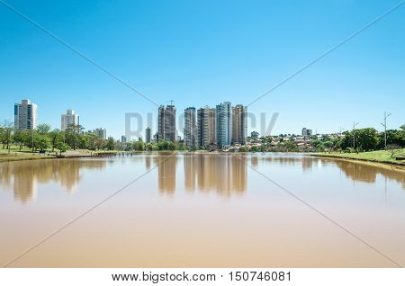 Park lake with vegetation, trees and some buildings in the background. Beautiful sunny day with reflection in water and a blue sky gradient. South America park, to relax with this beautiful view.
