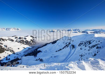 View To Alpine Mountains Surrounded By Fog And Ski Slopes In Austria From Kitzbuehel Ski Resort With