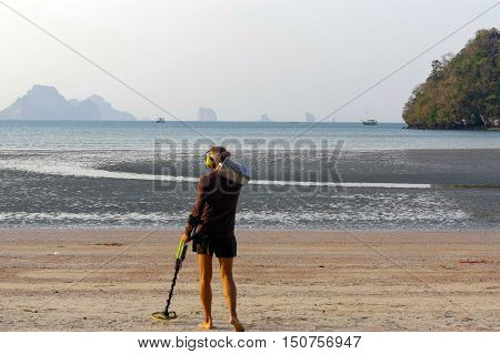 a treasure hunter with Metal detector on sunrise on the beach