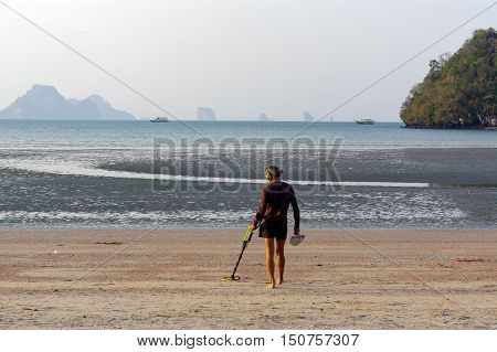 a treasure hunter with Metal detector on sunrise on the beach