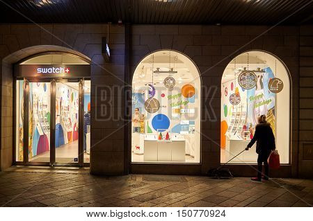 GENEVA, SWITZERLAND - NOVEMBER 18, 2015: woman looking in a shop window at night. A shop window is a window in a shop displaying items for sale or otherwise designed to attract customers to the store.
