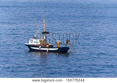 Fisherman on a small blue and white boat with fishing net between the waves of the sea. Liguria Italy