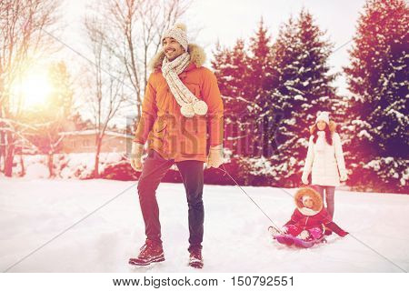 parenthood, fashion, season and people concept - happy family with child on sled walking in winter outdoors
