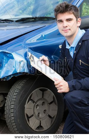 Auto Workshop Mechanic Inspecting Damage To Car And Filling In Repair Estimate