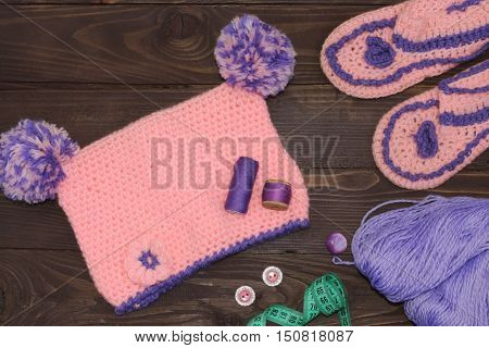 Knitted baby cap and Slippers, yarn for knitting on wooden table. The view from the top. Sewing accessories.
