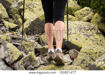 Woman hiking in mountains adventure and exercising. Legs and nordic walking poles in nature. Young fitness woman legs walking on mountains hike. Close-up of shoes and trekking poles on mountains
