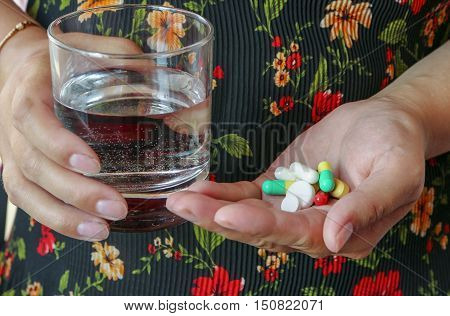 the young woman holds in hands pills and glass of water