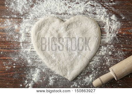 Pizza dough in heart shape with flour on table