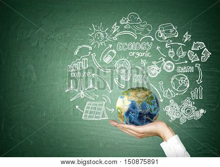 Close up of man's hand holding globe surrounded by sketches of renewable energy sources. Concept of being responsible. Mock up.