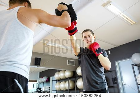 Low angle view of young male boxer punching bag held by instructor in gym