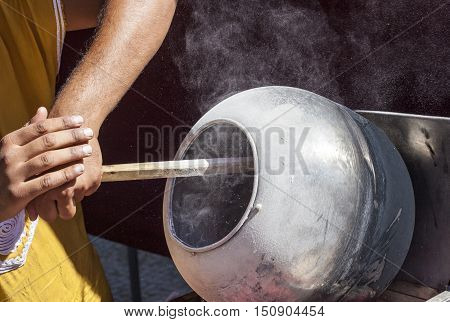 Man preparing sunflower seeds coated in caramel with long wooden spoon in a rotatory pot