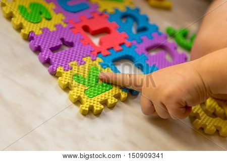 Colorful foam puzzle letters and numbers in kid's hands on a light table. Baby puts puzzle of letters and numbers. Close-up