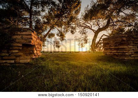 The ruins of an ancient wall open a door on the grass at sunset