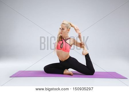 Young blonde slim girl is stretching in the studio on the white background