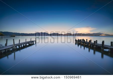 Two Wooden pier or jetty on a blue lake sunset and cloudy sky reflection on water. Long exposure Versilia Massaciuccoli Lake Tuscany Italy.
