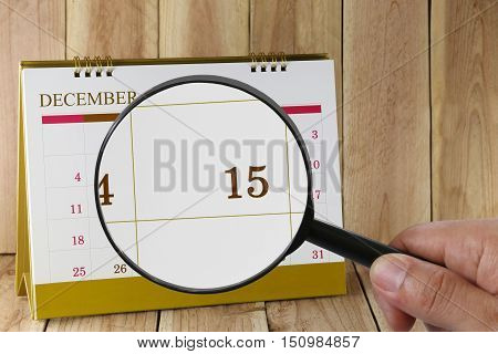 Magnifying glass in hand on calendar you can look Fifteenth date of monthFocus number fifteen in DecemberConcept in business and meetings.