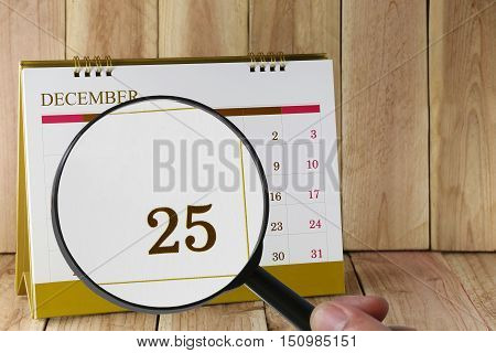 Magnifying glass in hand on calendar you can look Twenty Five date of monthFocus number Twenty Five in DecemberConcept in business and meetings.