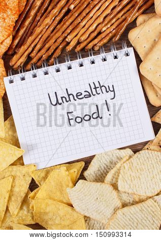 Inscription Unhealthy Food In Notebook And Heap Of Crisps And Cookies
